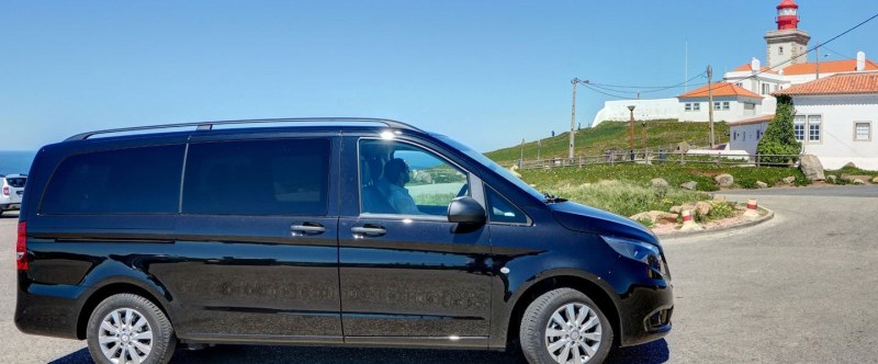 Black van parked near a lighthouse with blue sky in the background.